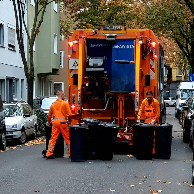 Zwei Mitarbeiter der Awista heben Mülltonnen in einem Müllwagen.