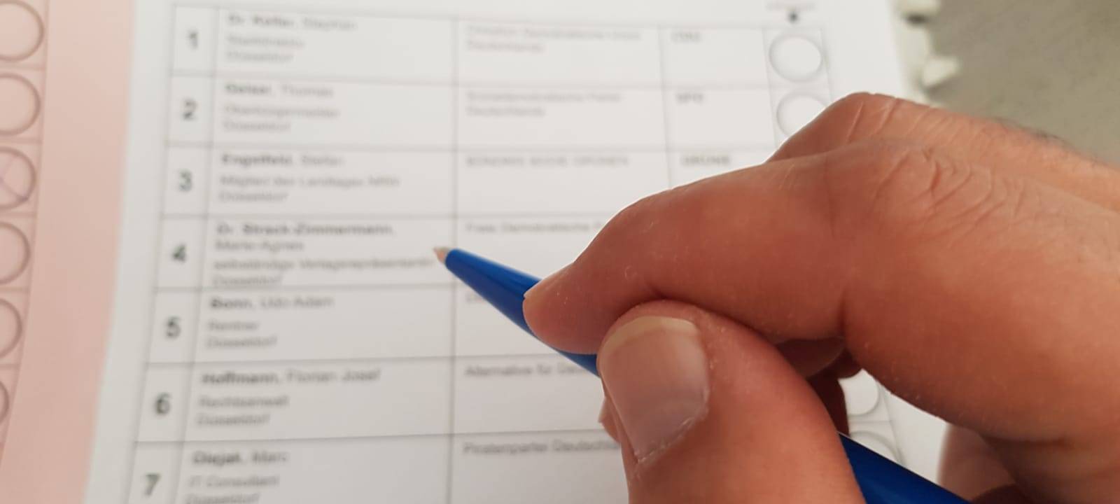 Eine Person hält einen Bleistift in der Hand und macht gleich ein Kreuzchen auf einem Wahlzettel.