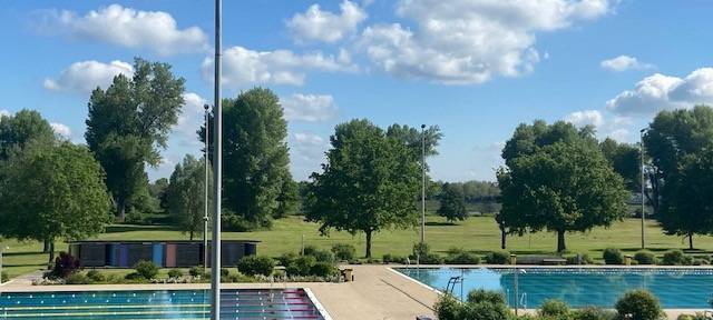 Freibad bei Sonnenschein und einer Wiese im Hintergrund.