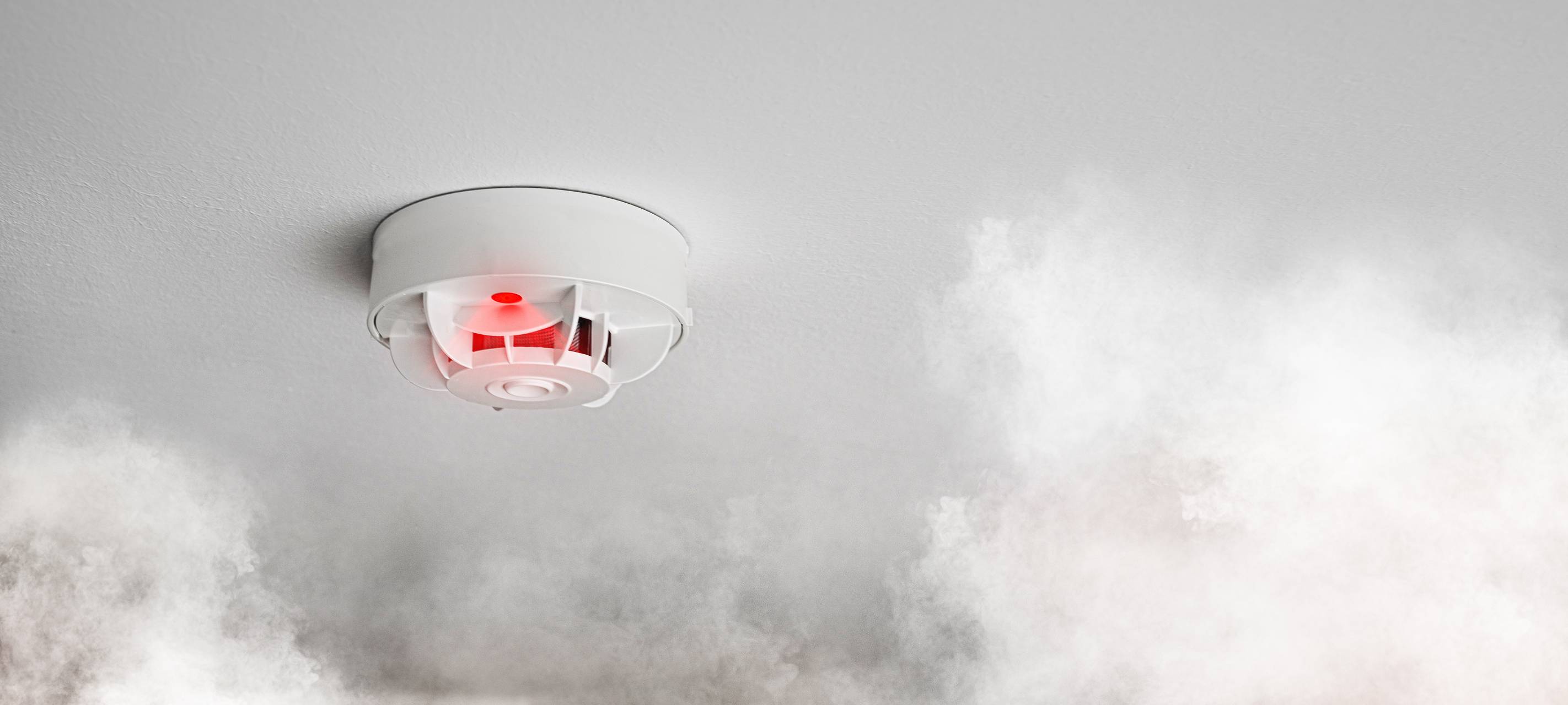 Ein Rauchmelder schlägt an, weil weißer Rauch im Raum zu sehen ist.