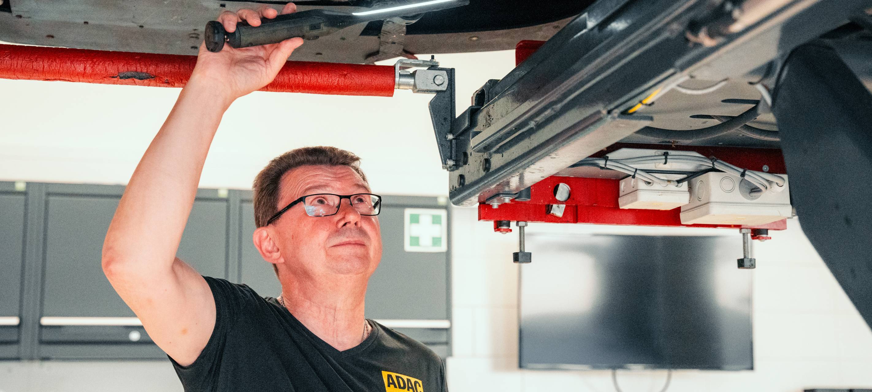Ein Auto ist auf der Hebebühne, ein ADAC-Mitarbeiter prüft