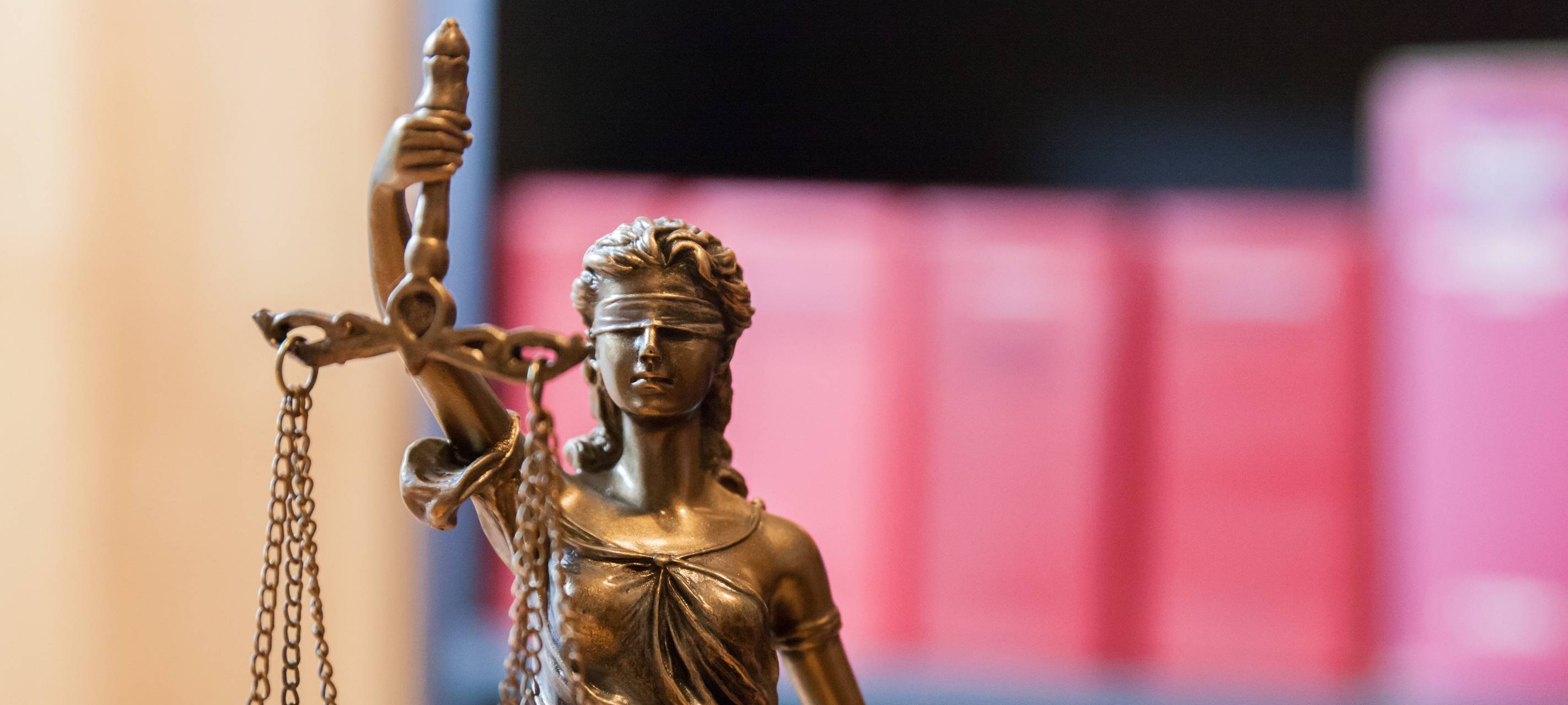 Justitia vor einem Bücherregal mit Gesetzbüchern.