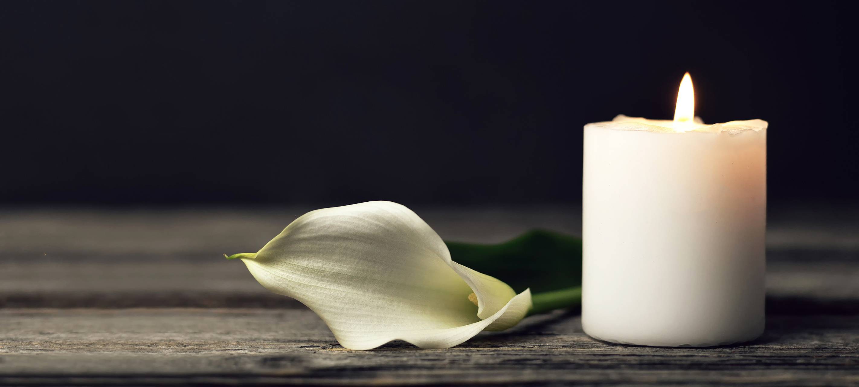 Brennende Kerze und weiße Calla-Lilie auf dunklem Hintergrund.