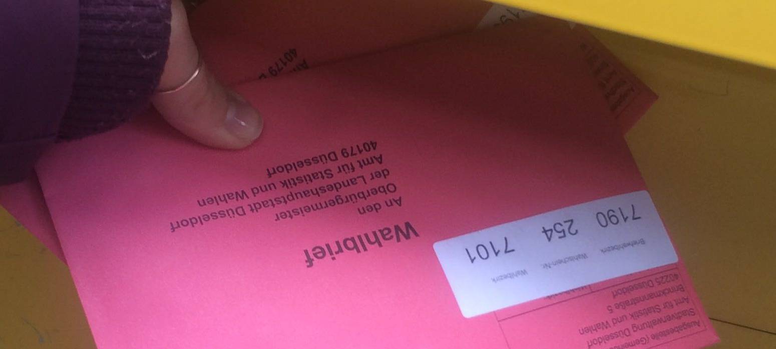 Ein rosa Briefumschlag wird in den Briefwahl gesteckt. Hier wird Briefwahl gemacht.