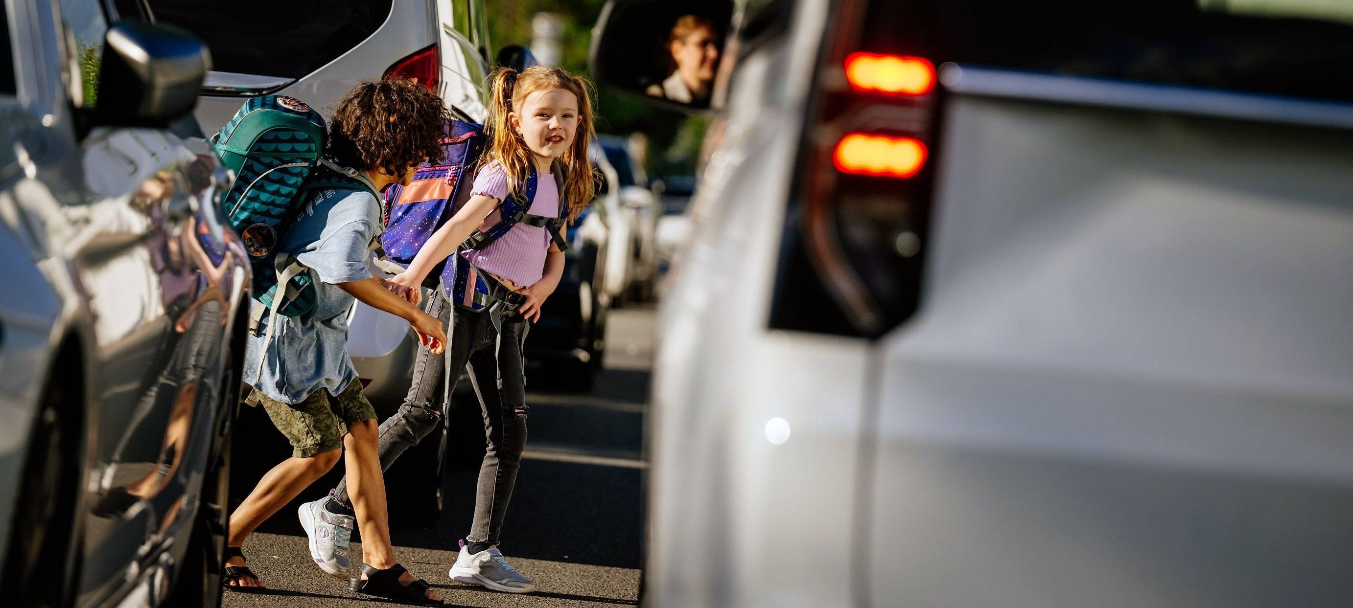 Zwei Kinder laufen zwischen Autos zur Schule